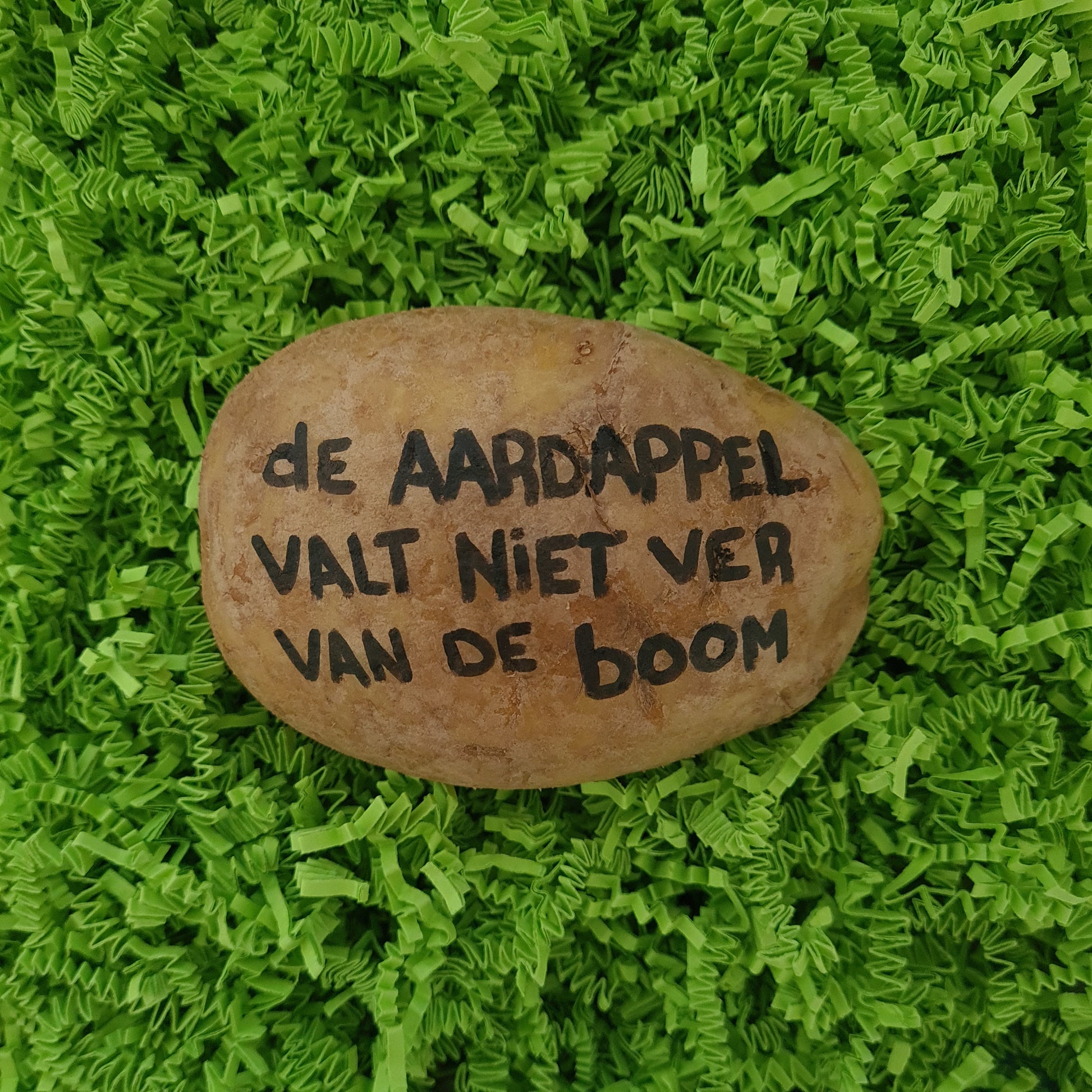 Een aardappel met daarop handgeschreven "de aardappel valt niet ver van de boom" in zwarte inkt. in hysterisch groene verpakking.