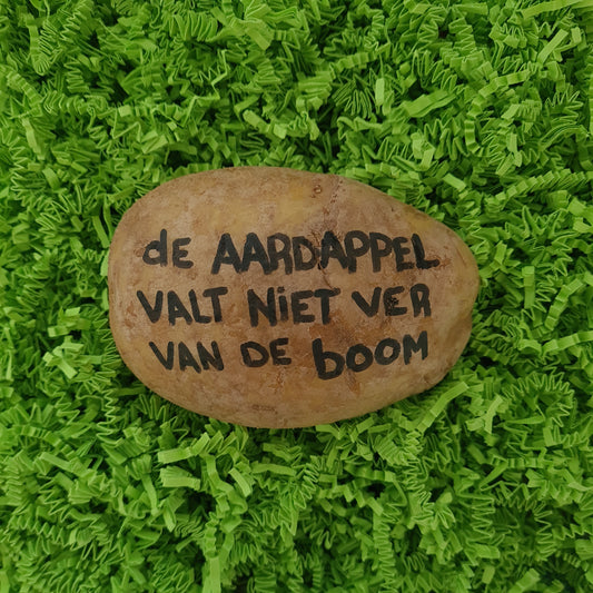 Een aardappel met daarop handgeschreven "de aardappel valt niet ver van de boom" in zwarte inkt. in hysterisch groene verpakking.